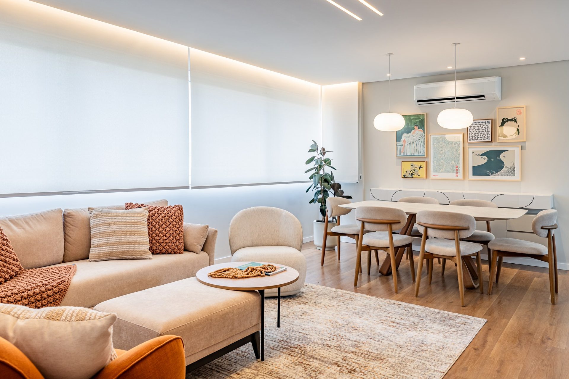 Living integrado com sala de jantar, sofá claro, almofadas em tons de terracota e mesa redonda